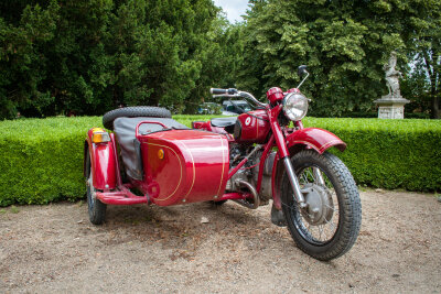 Ein rotes Ural-Motorrad steht vor einer Hecke.