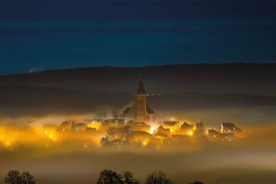 Beleuchtete Häuser mit Kirche bei Nacht im Nebel