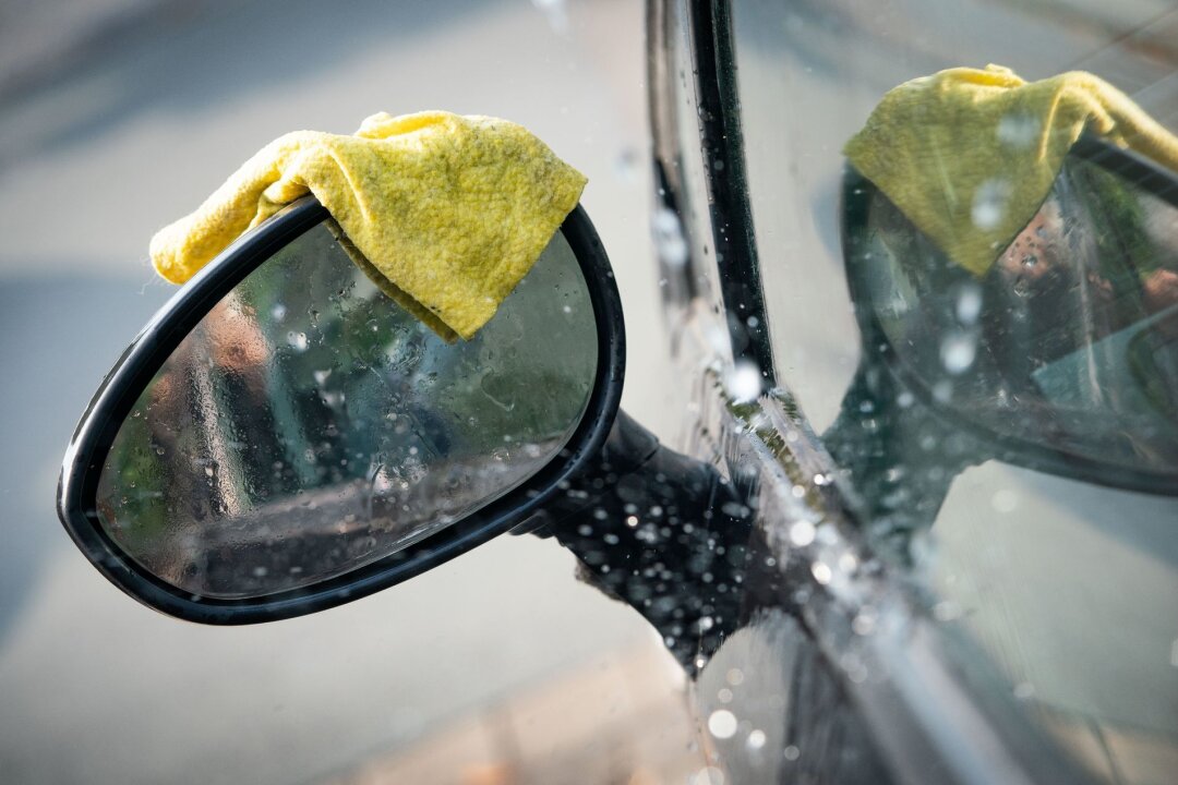 Mann entert Auto von älterem Ehepaar aus Waschbox - Illustration - Ein Lappen liegt während einer Autowäsche auf dem Seitenspiegel eines Fahrzeugs.