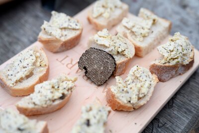 Trüffelgenuss perfekt: Tipps für den Kauf und die Zubereitung der exklusiven Delikatesse - Der Burgundertrüffel, (Tuber unicatum) gilt ebenfalls als Delikatesse. Hier liegt ein Stück in der Mitte eines Holzbretts zwischen Appetithäppchen mit Trüffelbutter. 