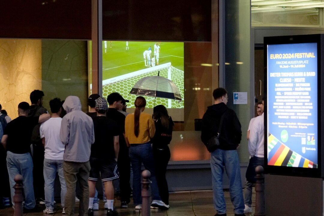 Unwetter am Freitag in Leipzig möglich - Fanzone betroffen? - Fußballfans stehen vor dem Fenster eines Hotels und verfolgen das Spiel.